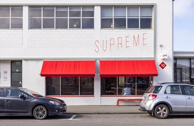 White brick exterior of cafe Supreme Supreme, with bright red awning.