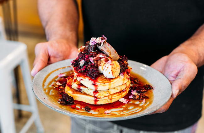 Man holding a plate of hotcakes with berries from t bay cafe, Porirua.