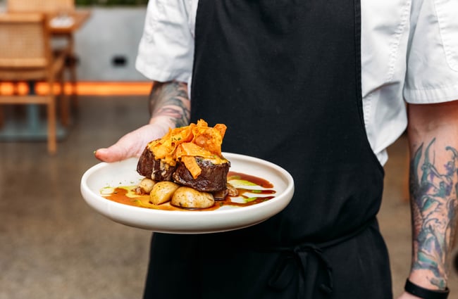 A chef holding a plate of steak.
