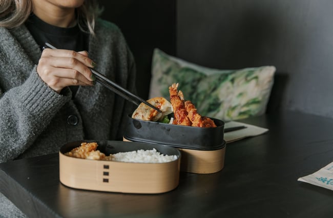 Hands holding chopsticks reaching for food on a plate.