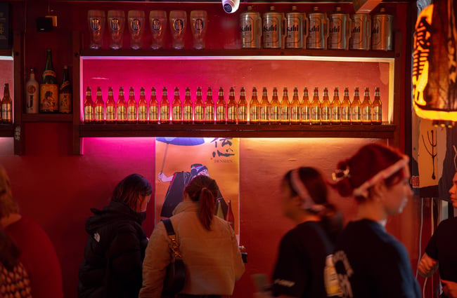Bottles of liquor lined up on a shelf above customers.