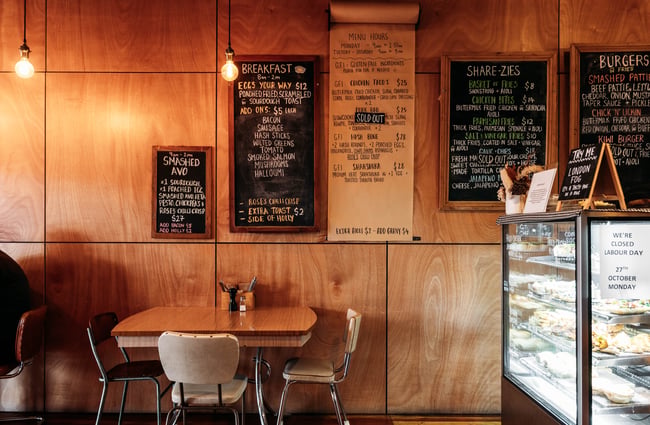 A set of table and chairs beneath the menu on the wall next to the food cabinet at Taper.