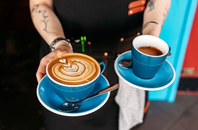 A staff member holds two coffees in their hands at Taper.