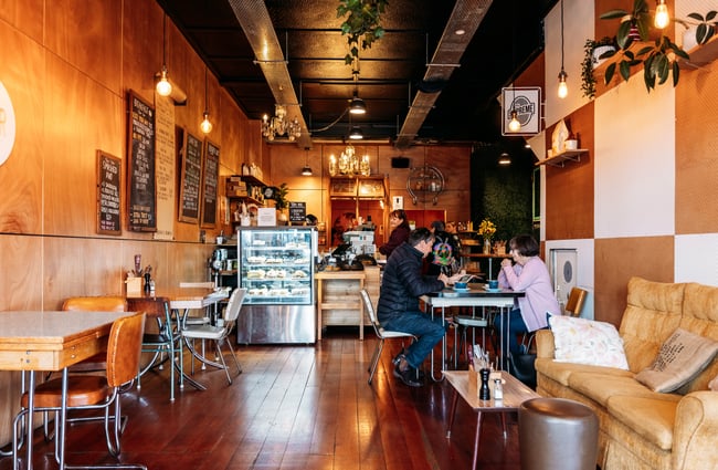 Customers sitting at tables in the cafe with cabinet and front counter behind them at Taper Eatery.