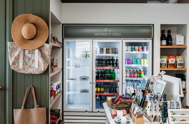 Drinks fridge in the store with hats hanging up at the side at Tarras Village.