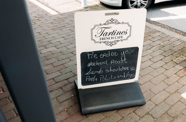 Sign outside cafe that reads "Pre-order your weekend roast: lamb shoulder with perla potatoes and veggies"