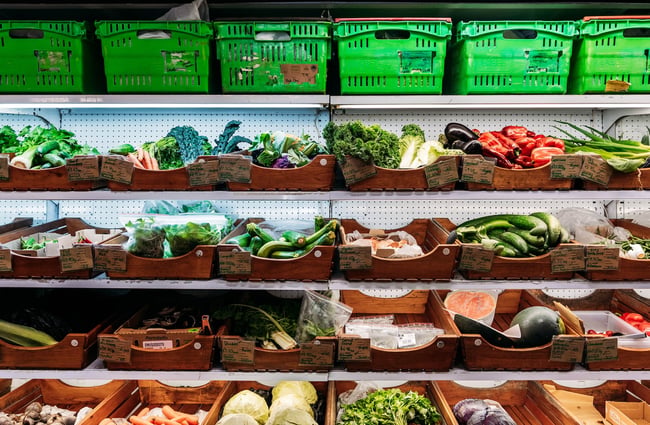 A full shelf of green vegetables in wooden boxes.