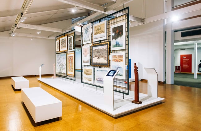 The gallery interior with a wire gridded wall coved in art work.
