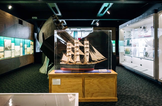 An old ship in a protective glass container on a wooden base.