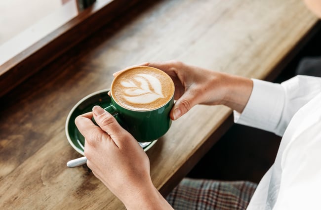 Someone holding a flat white coffee in a dark green cup