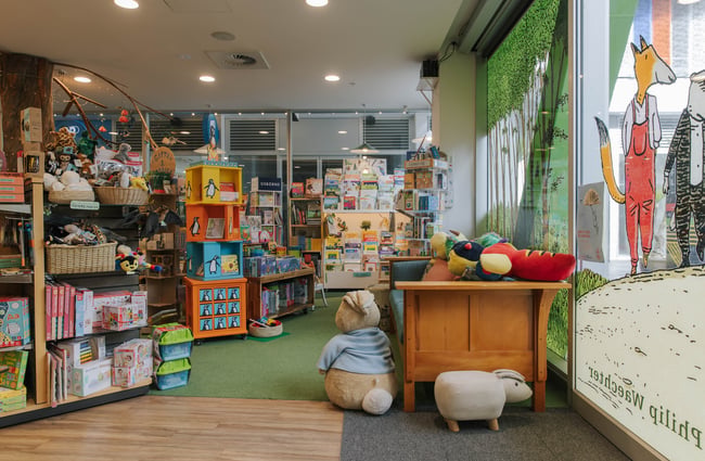 Books and toys on shelves and a couch with big soft toys at Telling Tales children's bookshop, Christchurch.