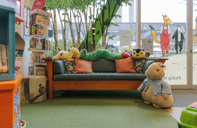 A large Peter Rabbit stuffed toy stands in front of a couch inside Telling Tales; other stuffed animals sit on the couch.