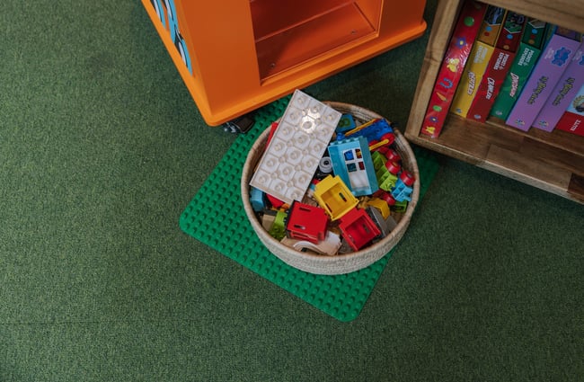Close up of a basket on the floor holding Lego building blocks for kids to play with.