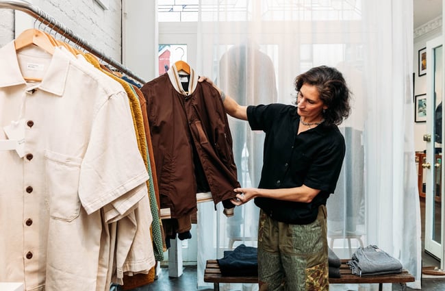 Shop assistant holding up a piece of clothing in that was then, this is now.
