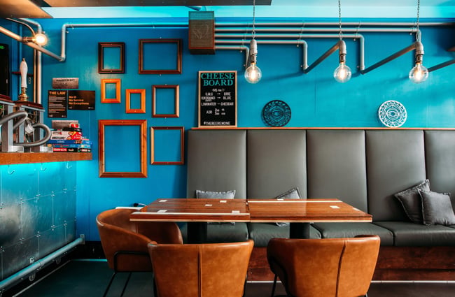 Tables up against grey padded wall seating and brown leather single chairs.
