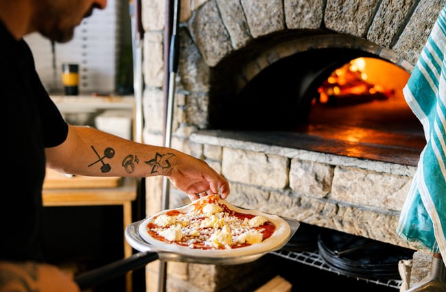 Chef placing a pizza onto the paddle to go into the woodfired oven.