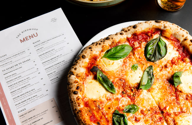 A close up of a pizza and the menu on a table at The Birdwood.