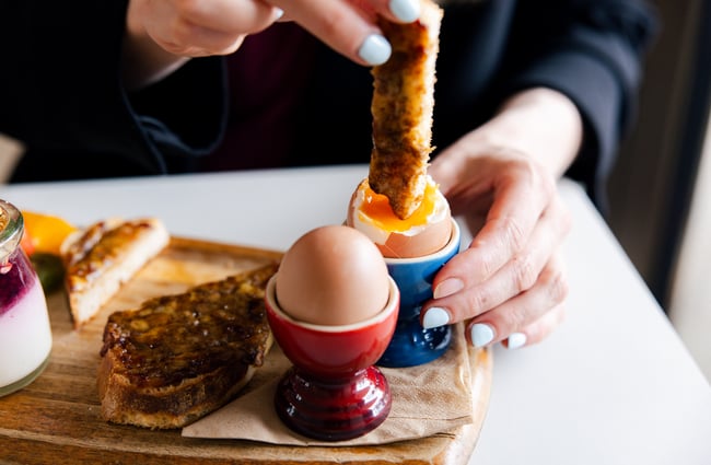 Customer dipping toast soldier into a soft boiled egg at The Birdwood.
