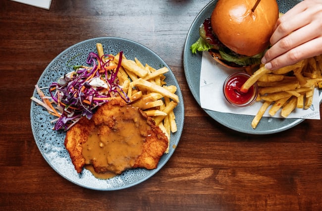 Flat lay of schnitzel and burger with someone dipping chip into tomato sauce