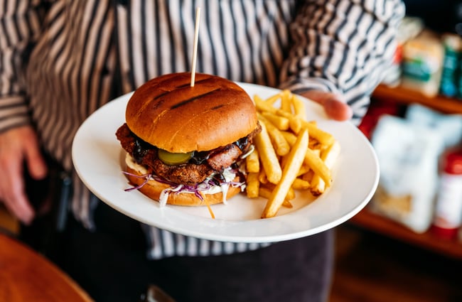 A hand holding a plate of chips and a burger at The Duke’s Roadhouse in Rangitikei.
