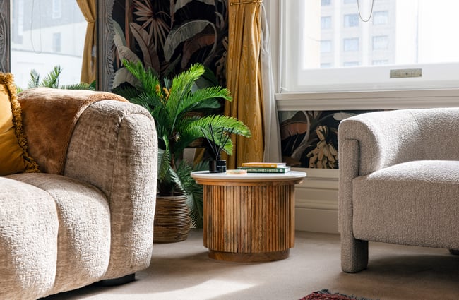 Round coffee table and plant in the background with sofas in the corner at The Eve Apartment.