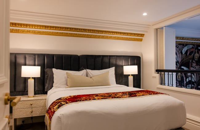 Leather headboard behind a luxuriously made bed, to the side is a balcony on the mezzanine bedroom at The Eve Apartment.