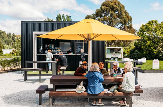 Customers sitting at an outdoor table under an umbrella at The Green.