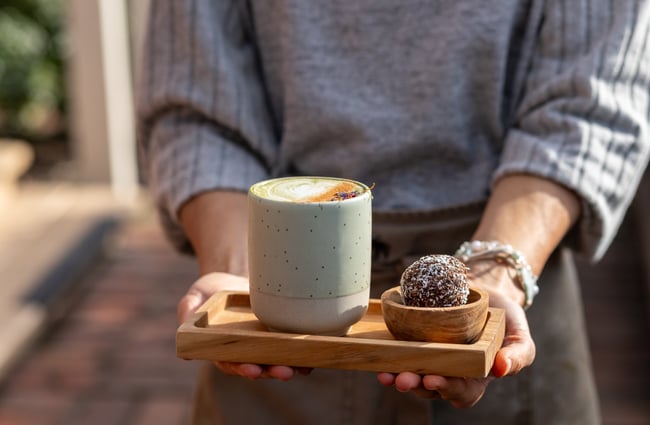 Barista delivering a hot drink and protein ball to a customer at The Lil Brew Espresso Bar.