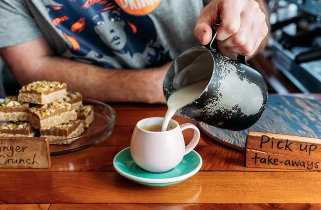 Close up of a barista pouring steamed milk into a coffee cup.