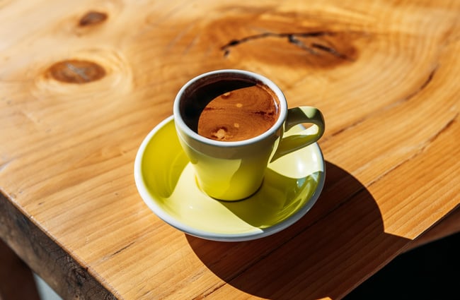 Close up of a black coffee in a yellow mug in the sun.