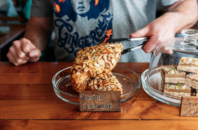 Close up of a staff member using tongs to pick up an almond croissant.