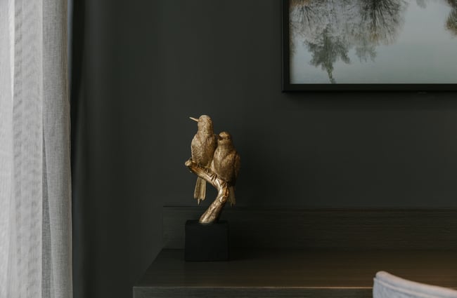 A close up of a gold bird sculpture next to a bed.