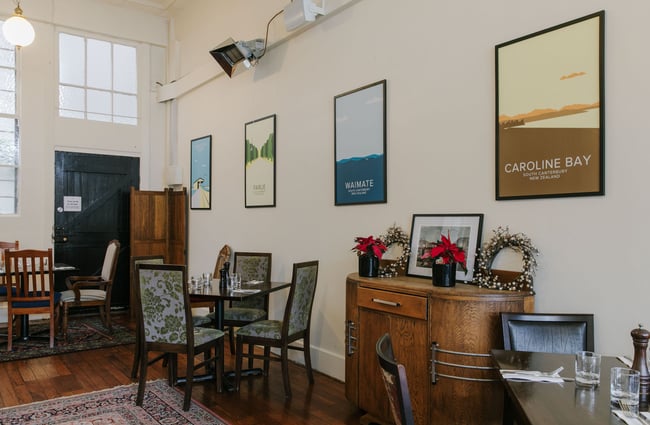 Colourful works of art on a wall next to brown wooden tables and chairs in The Oxford restaurant in Timaru.