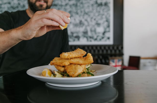Close up of fish on a plate with a chef squeezing lemon on top at The Oxford restaurant in Timaru.