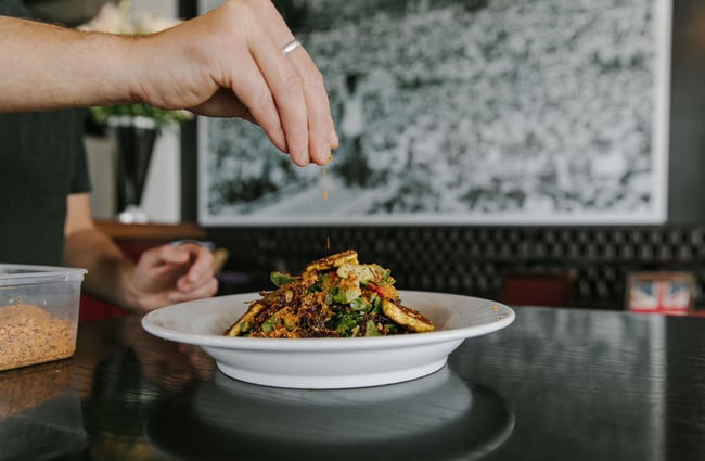 A close up of a halloumi salad with a chef hand sprinkling a topping on top at The Oxford restaurant in Timaru.