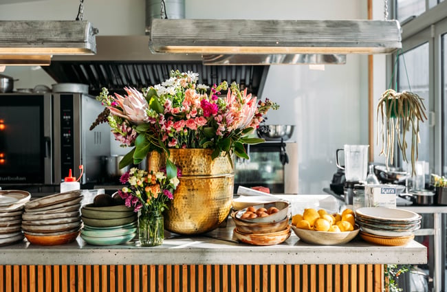 A kitchen counter full of bowls of fruit and vases of flowers.