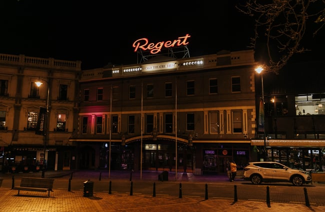 Exterior of theatre with neon sign at the top of the building.