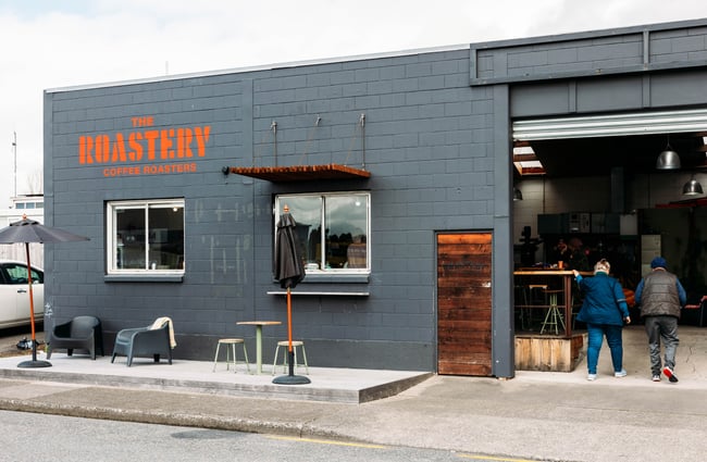 Warehouse building exterior with roller doors open and customers walking in to The Roastery.