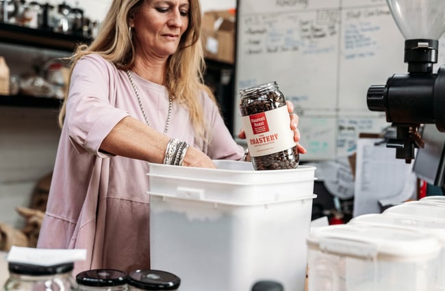 Woman scooping coffee beans out of a container into a jar at The Roastery.