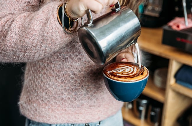 Barista pouring milk into coffee cup at The Roastery.