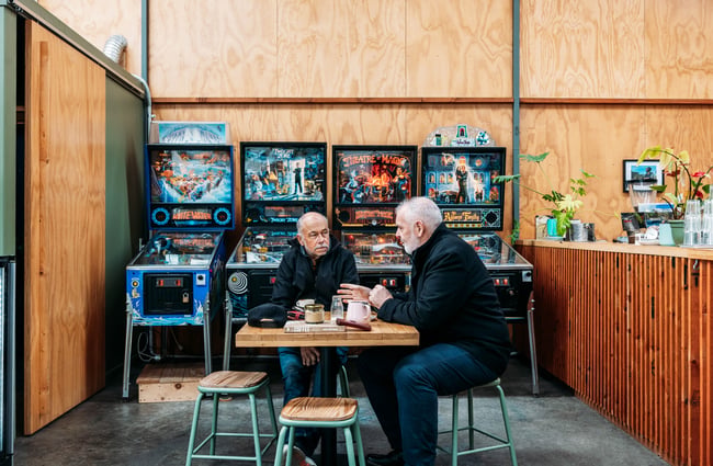 Customers sitting at a table with 80s gaming machines behind them at The Roastery.
