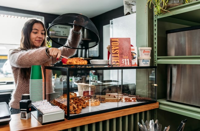 Woman behind the counter at the cafe picks up a scone from the cabinet at The Roastery.