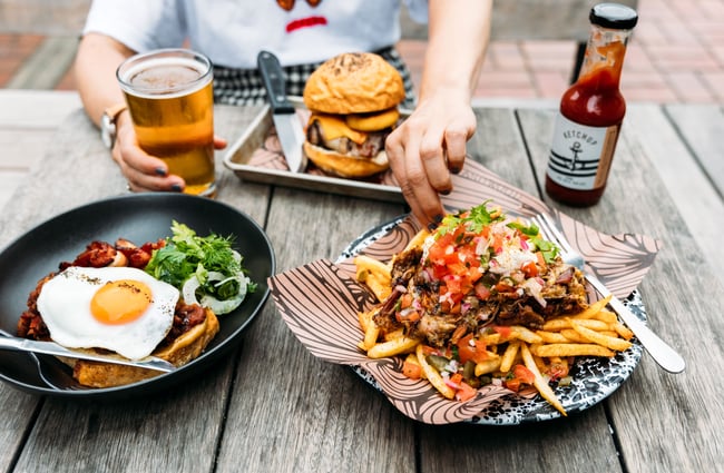 Loaded fries and other plates of food on an outdoor table.