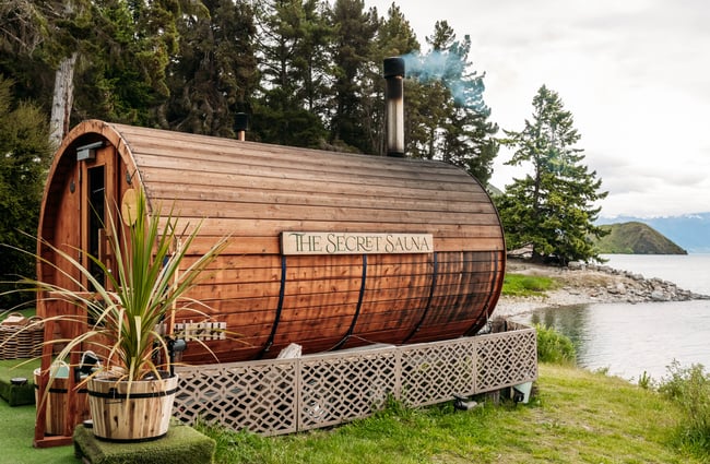 The wooden exterior of a sauna at a lake's edge.
