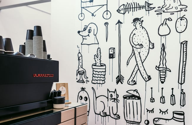 Red coffee machine with red writing against a black and white patterned wall.