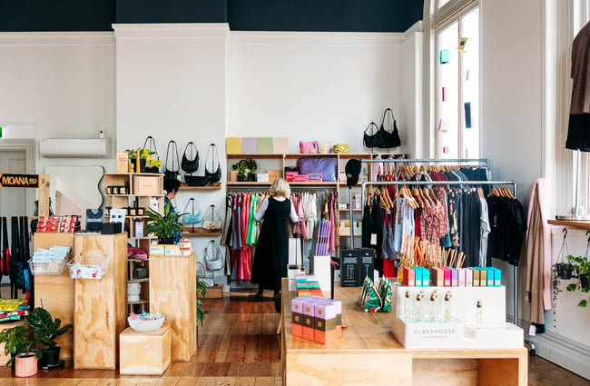 Woman browsing rack of clothing surrounded by shelves of homeware, accessories and fragrances