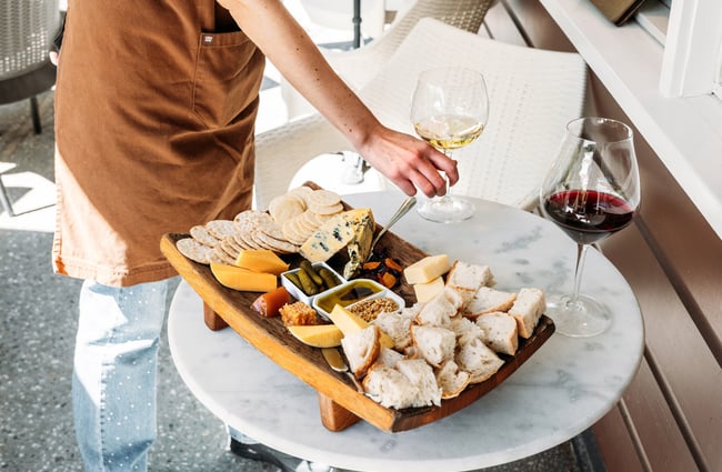 A cheese platter and wine on an outdoor table.