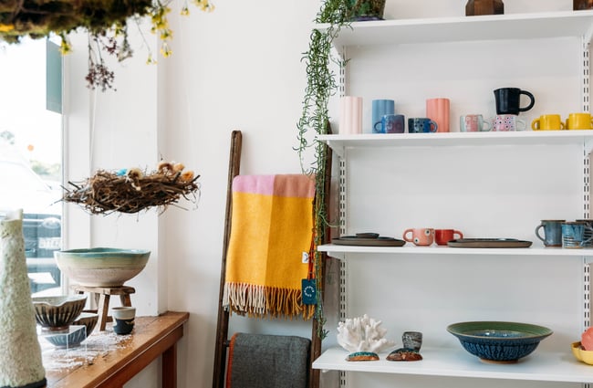 Ceramics on a shelving display, with a blanket ladder next to it and the window display at The Wobbly Pot.