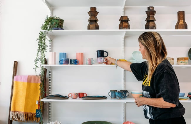 Shop owner arranges colourful ceramics on the shelf at The Wobbly Pot.