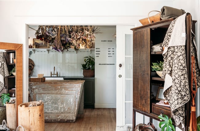 Looking past a wooden cabinet to another room where dried flowers hang above a floristry counter in The Workroom.